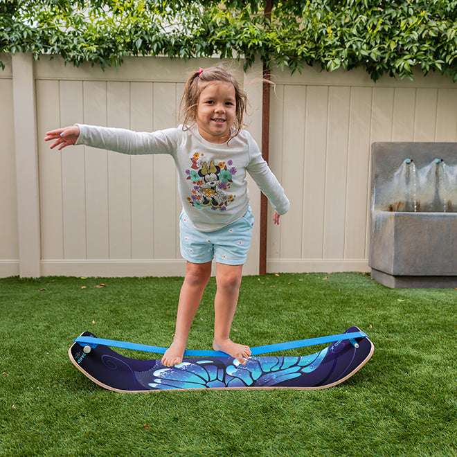 Child standing on a balance board in a backyard