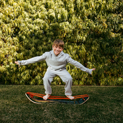 Child in a light gray outfit standing on a GIBBON Dino SlackBoard Plus with a green bushy background