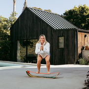 Woman standing on a GIBBON Dino SlackBoard Plus in front of a wooden cabin.